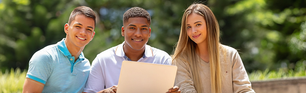 tres jóvenes sonriendo y trabajando juntos en un portátil al aire libre