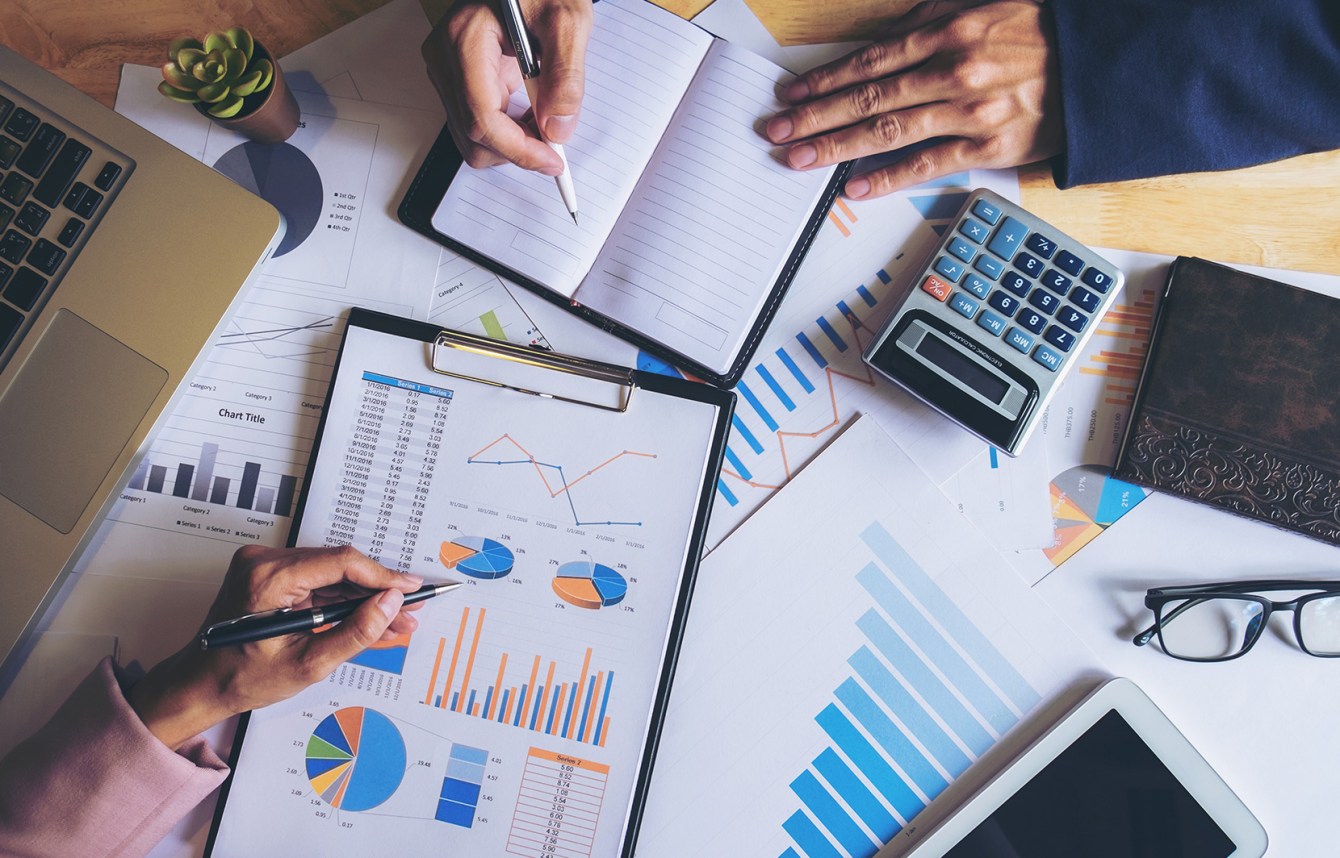 manos tomando nota mientras se analizan reportes financieros y métricas