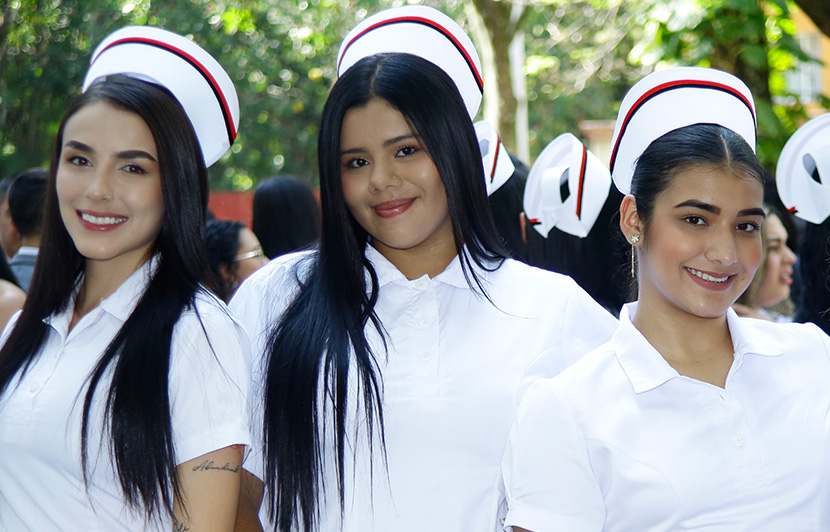 tres chicas estudiantes de enfermería con uniforme blanco y gorro en ceremonia académica