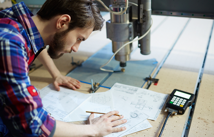 profesional en diseño de procesos industriales con planos y maquinaria CNC en laboratorio