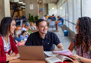 personas estudiando en una mesa con computadora portátil y material académico