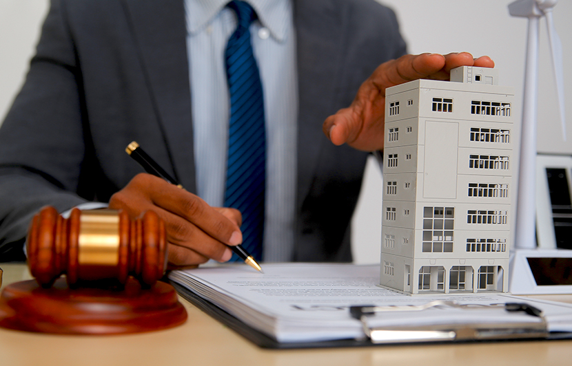 mesa con martillo judicial y edificio con alguien firmando documentos