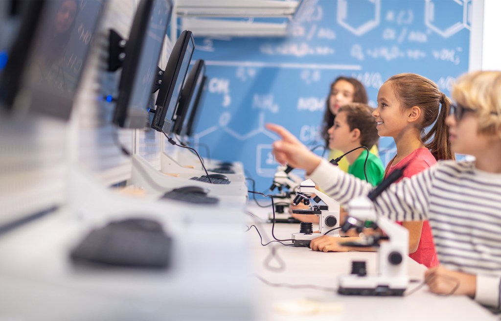 actividad educativa con niños usando computadoras y microscopios en aula escolar