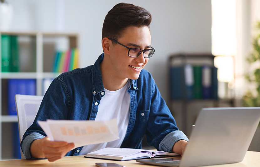 auxiliar financiero estudiando reportes impresos mientras trabaja en laptop