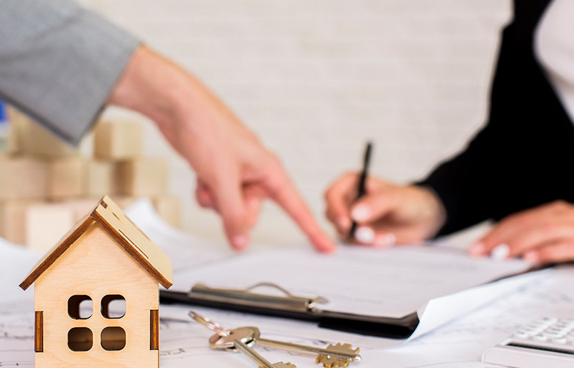 firma de documentos inmobiliarios con maqueta de casa y llaves sobre la mesa