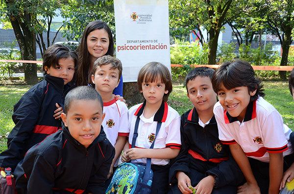 Grupo de estudiantes del Colegio están en una zona verde y posan para la foto con su profesora. Al fondo se encuentra el pendón de psicoorientación